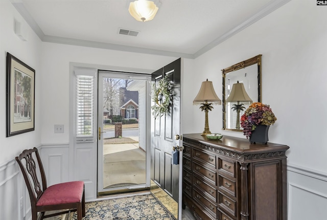 entryway featuring ornamental molding, a wainscoted wall, visible vents, and a decorative wall