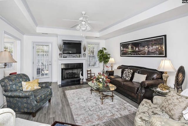 living room with plenty of natural light, crown molding, a tray ceiling, and wood finished floors