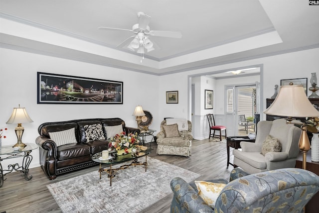 living area with a ceiling fan, a tray ceiling, crown molding, and wood finished floors