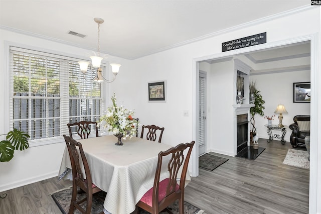 dining space featuring visible vents, a fireplace with raised hearth, wood finished floors, an inviting chandelier, and crown molding