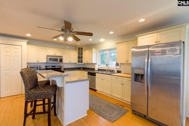 kitchen featuring appliances with stainless steel finishes, crown molding, light wood-style floors, and a kitchen island