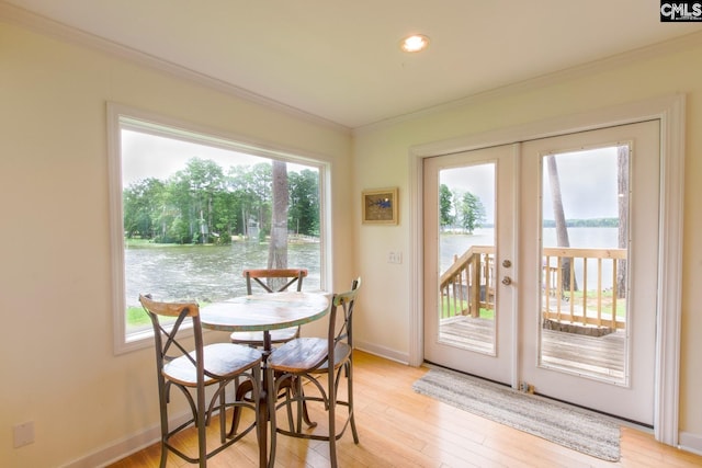 dining room with french doors, a water view, ornamental molding, light wood-style floors, and baseboards