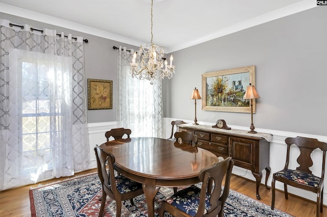 dining room with a chandelier, ornamental molding, wainscoting, and wood finished floors