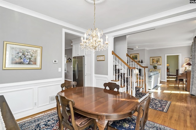 dining space featuring visible vents, wainscoting, stairway, ornamental molding, and wood finished floors