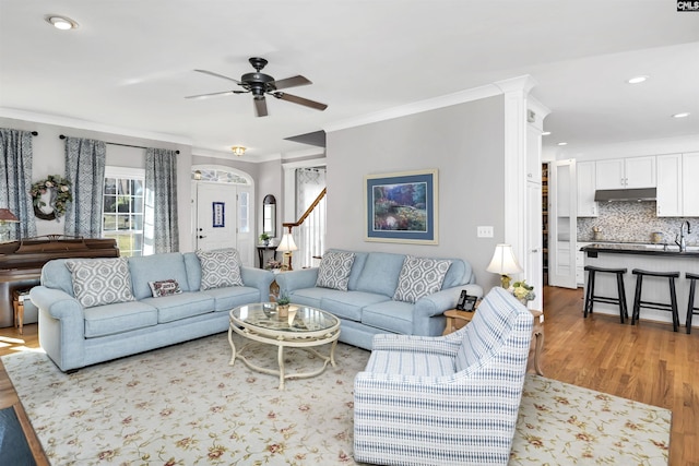 living room with arched walkways, crown molding, ceiling fan, wood finished floors, and stairs