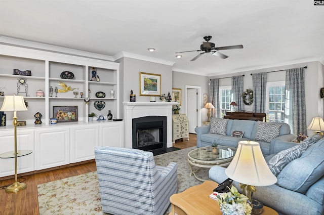 living area featuring a fireplace with flush hearth, ornamental molding, wood finished floors, and a ceiling fan