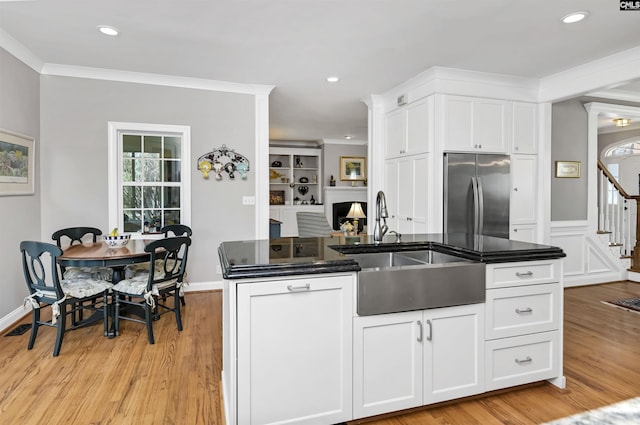 kitchen with ornamental molding, light wood-style floors, stainless steel fridge, and a sink