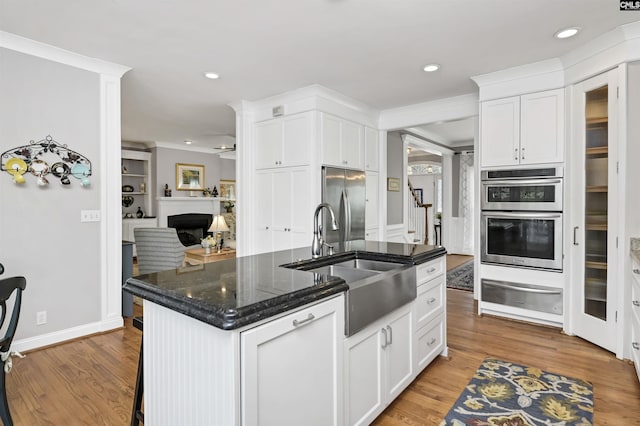 kitchen featuring a fireplace, a warming drawer, stainless steel appliances, a sink, and wood finished floors