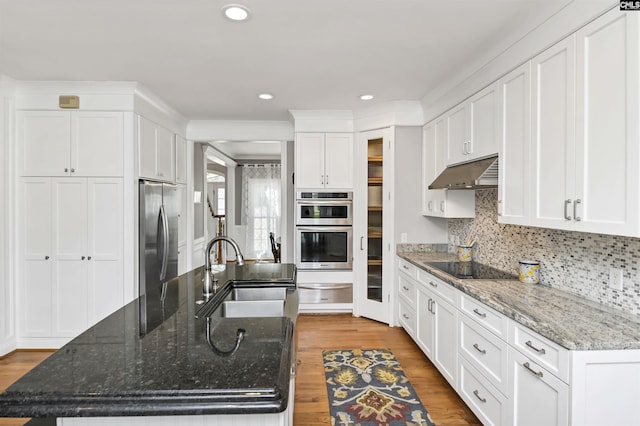 kitchen with white cabinets, appliances with stainless steel finishes, wood finished floors, under cabinet range hood, and a sink