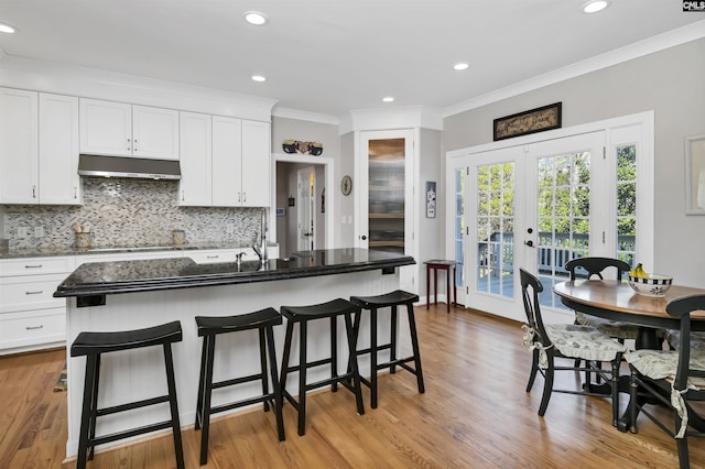 kitchen with under cabinet range hood, white cabinetry, a kitchen breakfast bar, french doors, and decorative backsplash