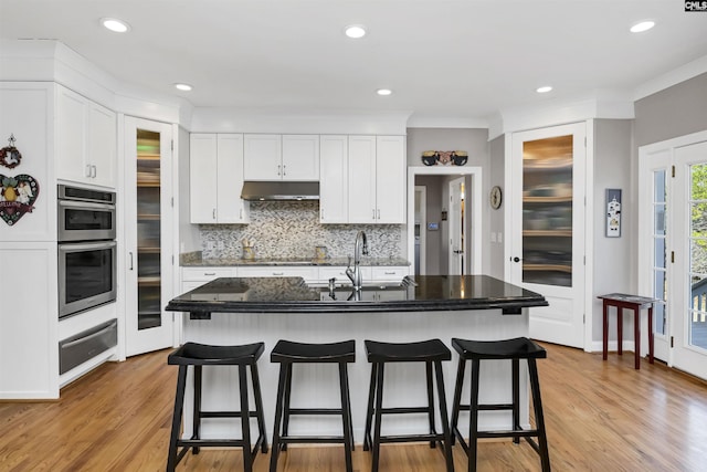 kitchen with a kitchen breakfast bar, under cabinet range hood, white cabinetry, a sink, and a warming drawer