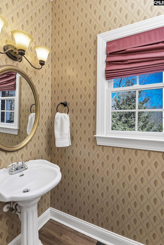 bathroom featuring baseboards, a sink, wood finished floors, and wallpapered walls