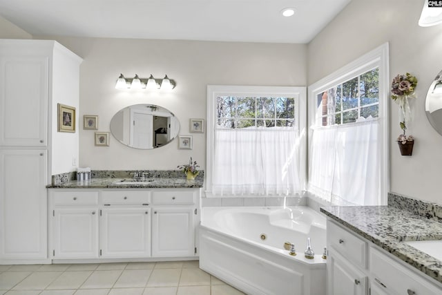 bathroom with a tub with jets, two vanities, tile patterned flooring, and a sink