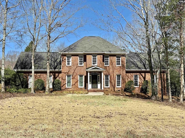 view of front facade featuring roof with shingles, a front lawn, and brick siding