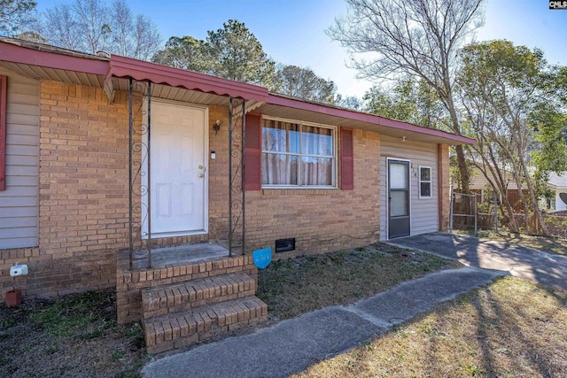 doorway to property with crawl space, brick siding, and fence