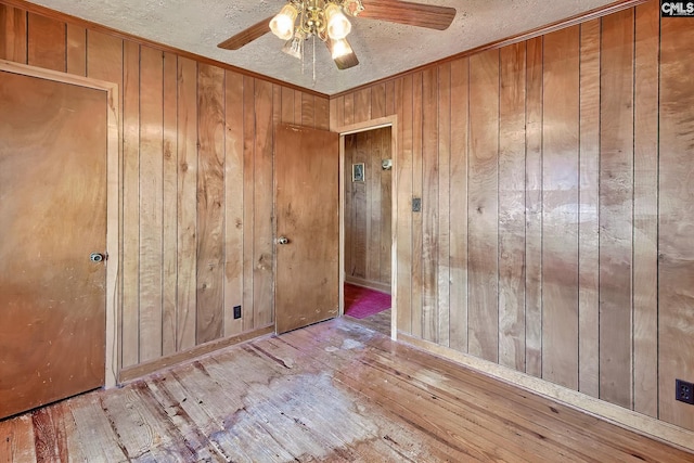 spare room featuring a ceiling fan, wood-type flooring, and wood walls