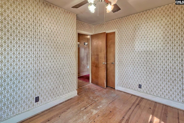 spare room with wallpapered walls, wood-type flooring, baseboards, and ceiling fan