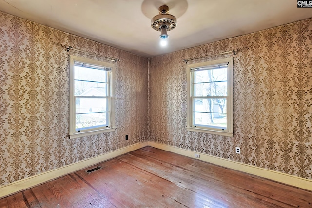 unfurnished room with wallpapered walls, baseboards, visible vents, and hardwood / wood-style floors