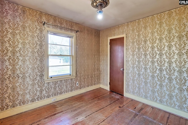 empty room featuring wallpapered walls, baseboards, and hardwood / wood-style flooring