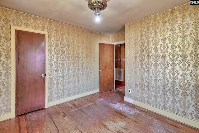 unfurnished room with baseboards, visible vents, hardwood / wood-style floors, and wallpapered walls