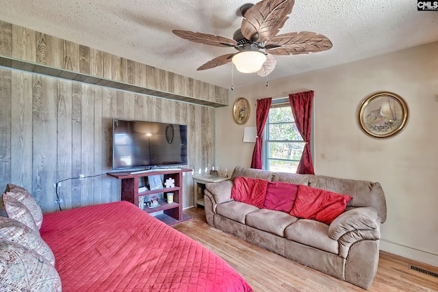 bedroom with wooden walls, visible vents, ceiling fan, wood finished floors, and a textured ceiling