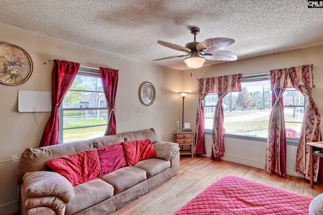 living room with light wood-style floors, ceiling fan, and a textured ceiling