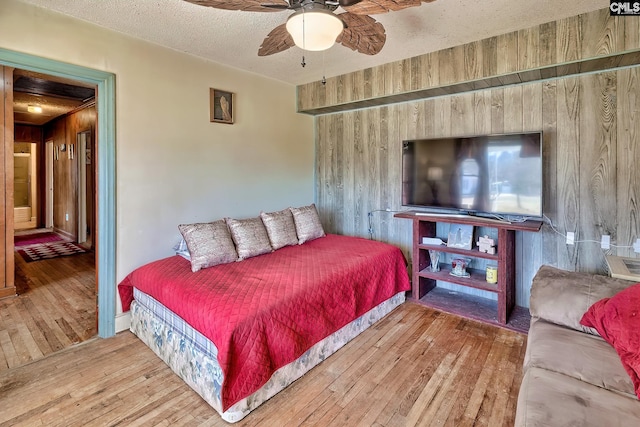 bedroom with ceiling fan, wooden walls, hardwood / wood-style floors, and a textured ceiling