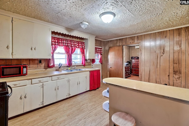 kitchen featuring wooden walls, stove, a sink, light countertops, and light wood-type flooring