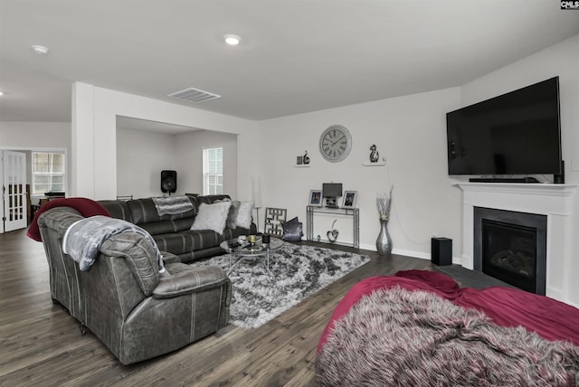 living room featuring visible vents, a fireplace with flush hearth, baseboards, and wood finished floors