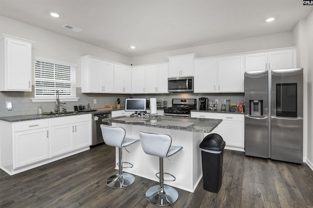 kitchen featuring visible vents, a sink, stainless steel appliances, white cabinets, and a center island