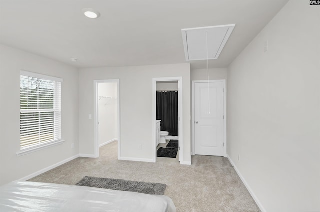 bedroom featuring a walk in closet, baseboards, attic access, carpet floors, and ensuite bath