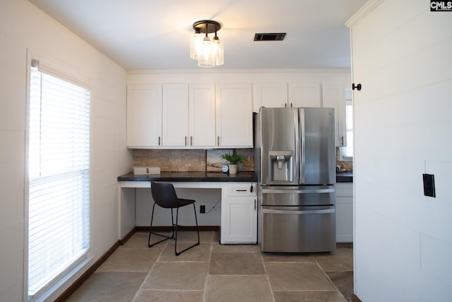 kitchen with visible vents, decorative backsplash, built in study area, dark countertops, and stainless steel fridge with ice dispenser