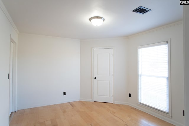 empty room with baseboards, visible vents, crown molding, and light wood finished floors