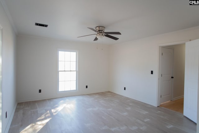 spare room with a ceiling fan, visible vents, baseboards, ornamental molding, and light wood finished floors