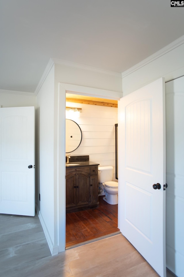 bathroom featuring baseboards, toilet, wood finished floors, crown molding, and vanity