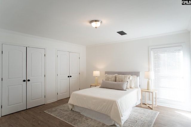 bedroom with ornamental molding, multiple closets, and wood finished floors