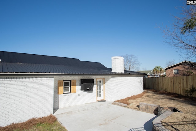 back of house with metal roof, brick siding, fence, a chimney, and a patio area