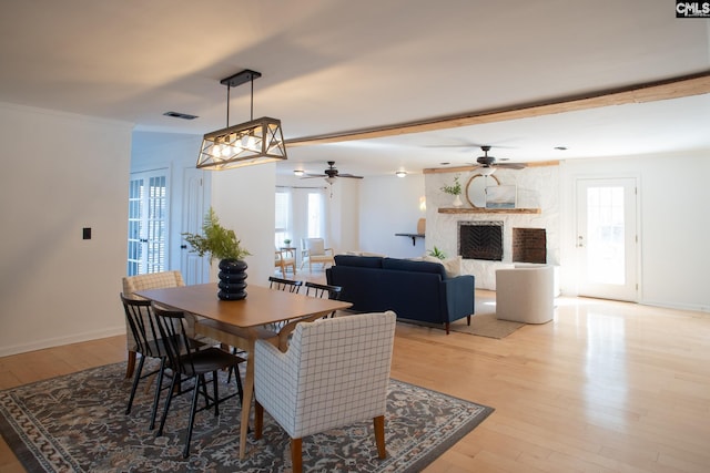 dining room with light wood-style floors, visible vents, a stone fireplace, and baseboards