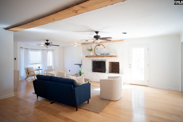 living room with light wood-style flooring, a fireplace, a ceiling fan, and beamed ceiling