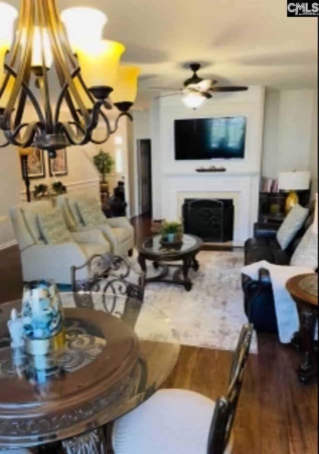 living room with a fireplace, wood finished floors, and ceiling fan with notable chandelier