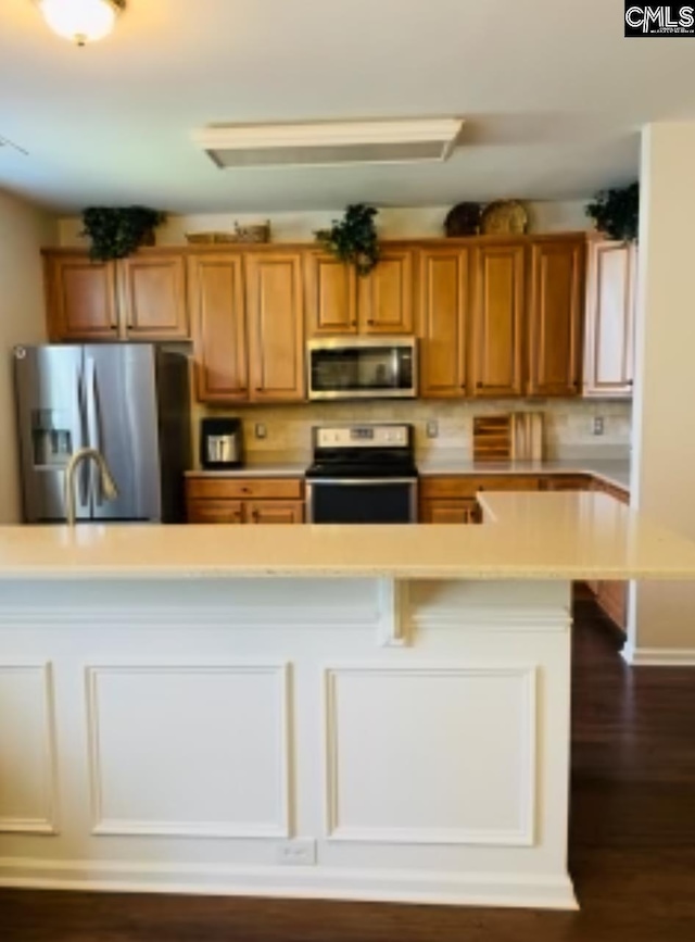 kitchen featuring appliances with stainless steel finishes, a breakfast bar, dark wood-style flooring, brown cabinets, and light countertops