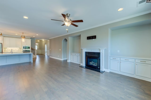 unfurnished living room featuring visible vents, arched walkways, ceiling fan, dark wood-style flooring, and a fireplace