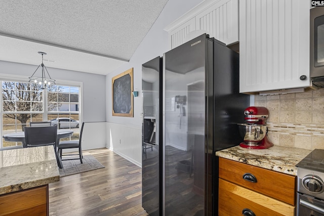 kitchen with a textured ceiling, a wainscoted wall, white cabinets, stainless steel refrigerator with ice dispenser, and dark wood finished floors