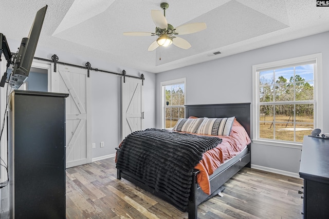 bedroom featuring a barn door, a textured ceiling, visible vents, and wood finished floors