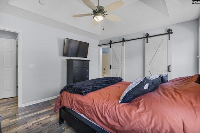 bedroom with a textured ceiling, a barn door, wood finished floors, and baseboards