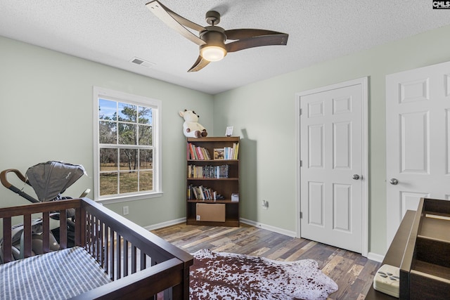 bedroom featuring a textured ceiling, wood finished floors, a ceiling fan, visible vents, and baseboards