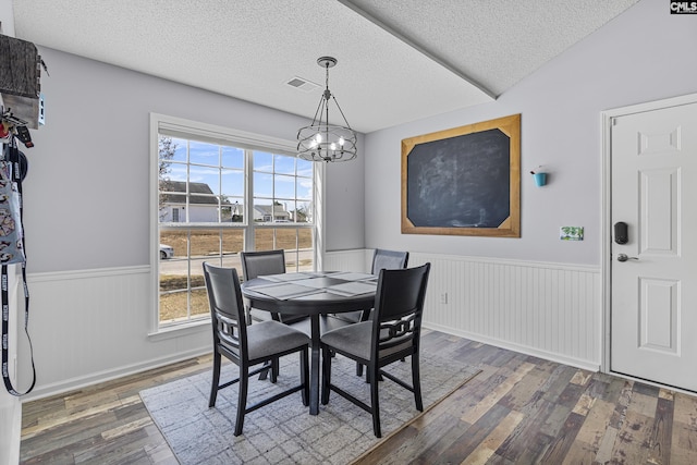 dining space with a textured ceiling, a notable chandelier, visible vents, wainscoting, and wood-type flooring