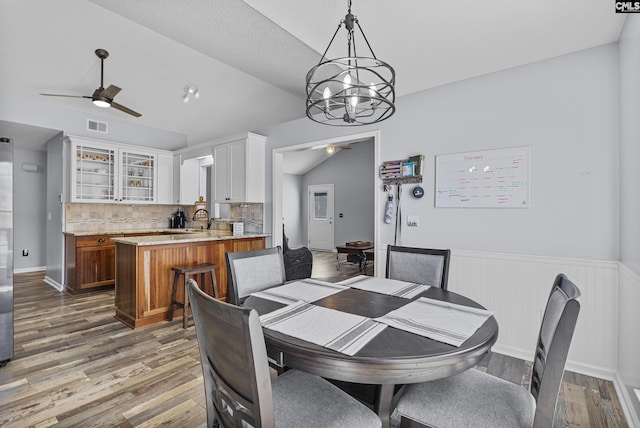 dining space featuring light wood-style floors, visible vents, vaulted ceiling, and ceiling fan with notable chandelier