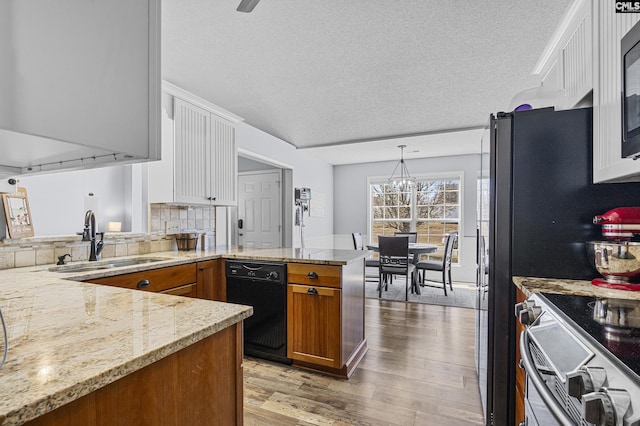 kitchen with brown cabinetry, wood finished floors, a peninsula, black appliances, and a sink