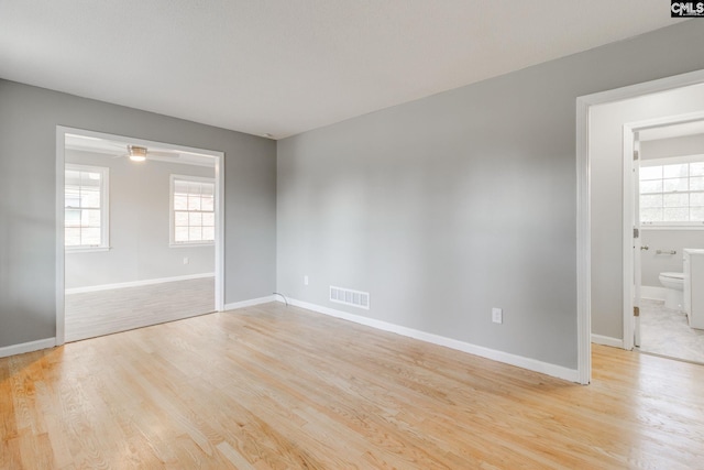 unfurnished room with light wood-style floors, visible vents, plenty of natural light, and baseboards